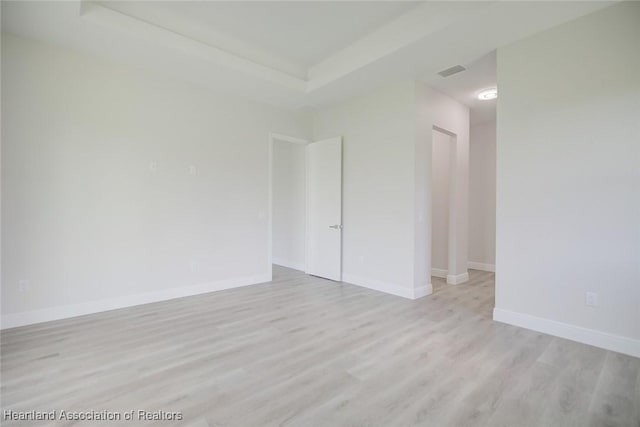 spare room with a raised ceiling and light hardwood / wood-style flooring