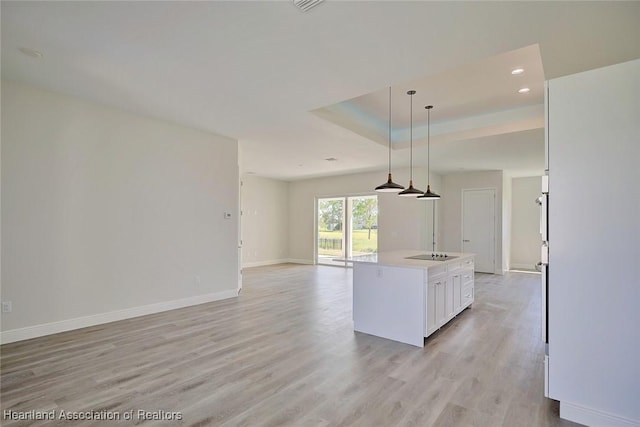 kitchen featuring white cabinetry, hanging light fixtures, an island with sink, black electric cooktop, and light wood-type flooring