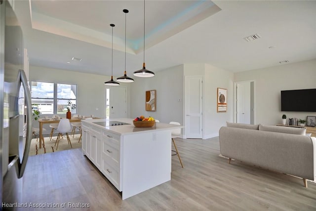 kitchen featuring stainless steel refrigerator, hanging light fixtures, a kitchen island, a raised ceiling, and white cabinets