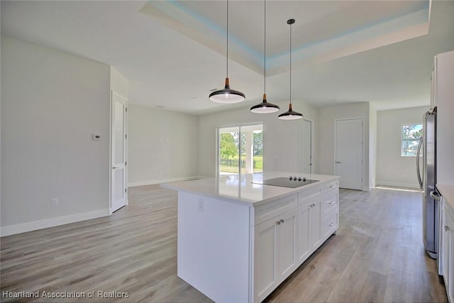 kitchen with black electric cooktop, a raised ceiling, a kitchen island, pendant lighting, and white cabinetry