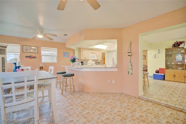 kitchen with white cabinetry, ceiling fan, kitchen peninsula, stove, and a kitchen bar