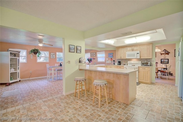 kitchen featuring light brown cabinets, white appliances, ceiling fan, kitchen peninsula, and a breakfast bar area