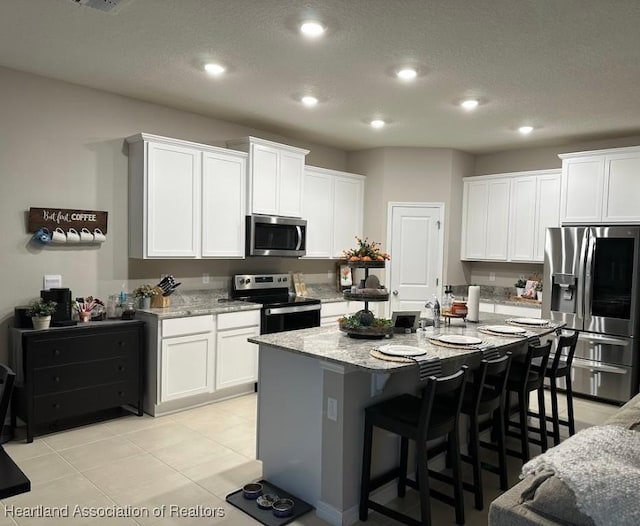 kitchen with appliances with stainless steel finishes, light tile patterned floors, white cabinetry, and light stone counters