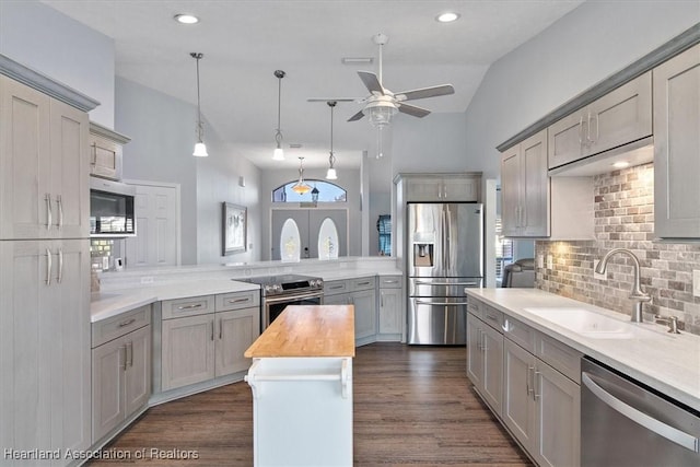 kitchen with kitchen peninsula, appliances with stainless steel finishes, backsplash, vaulted ceiling, and sink