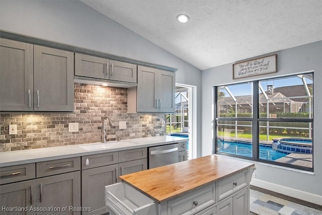 kitchen featuring decorative backsplash, stainless steel dishwasher, a textured ceiling, vaulted ceiling, and sink