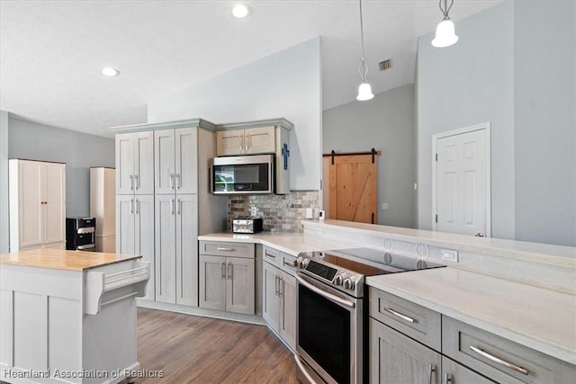 kitchen featuring gray cabinetry, a barn door, decorative light fixtures, decorative backsplash, and appliances with stainless steel finishes