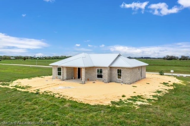 rear view of house with a rural view, concrete block siding, a lawn, and metal roof