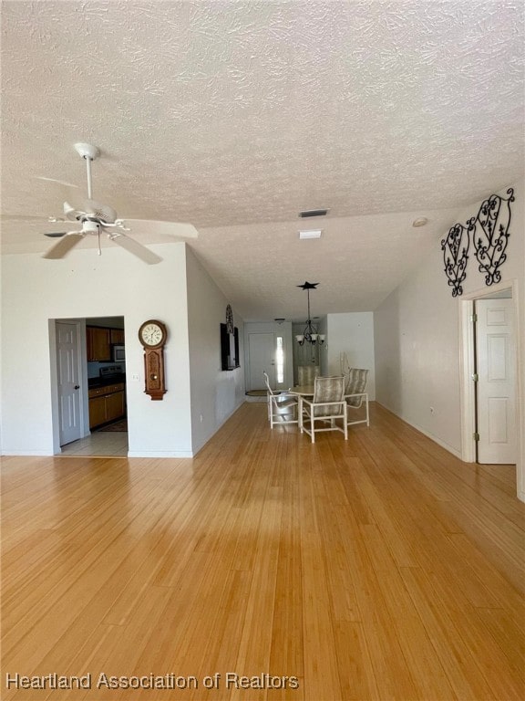 unfurnished dining area with lofted ceiling, ceiling fan with notable chandelier, a textured ceiling, and light wood-type flooring