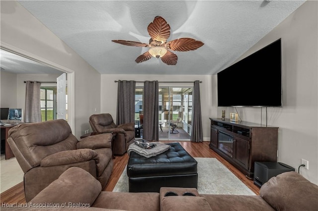 living room with ceiling fan, light hardwood / wood-style floors, lofted ceiling, and a textured ceiling