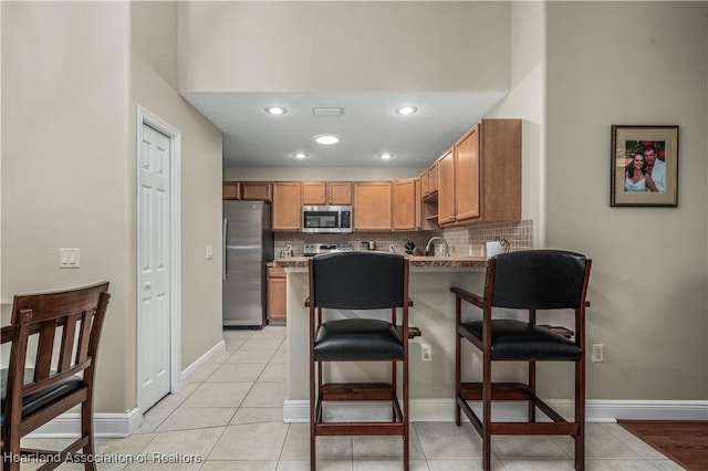 kitchen featuring decorative backsplash, stainless steel appliances, sink, light tile patterned floors, and a breakfast bar area