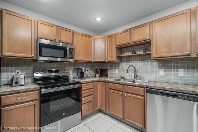 kitchen with sink, light tile patterned floors, a textured ceiling, appliances with stainless steel finishes, and tasteful backsplash