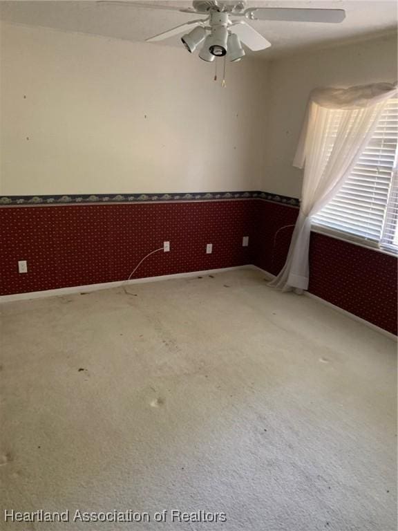 carpeted spare room featuring baseboards, ceiling fan, wainscoting, and wallpapered walls