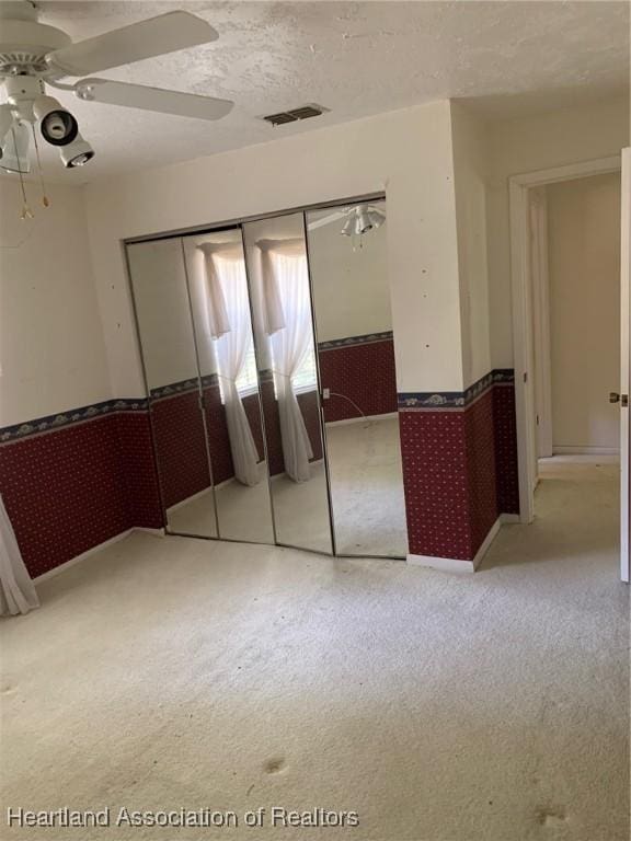 unfurnished bedroom featuring wainscoting, carpet floors, wallpapered walls, visible vents, and a closet