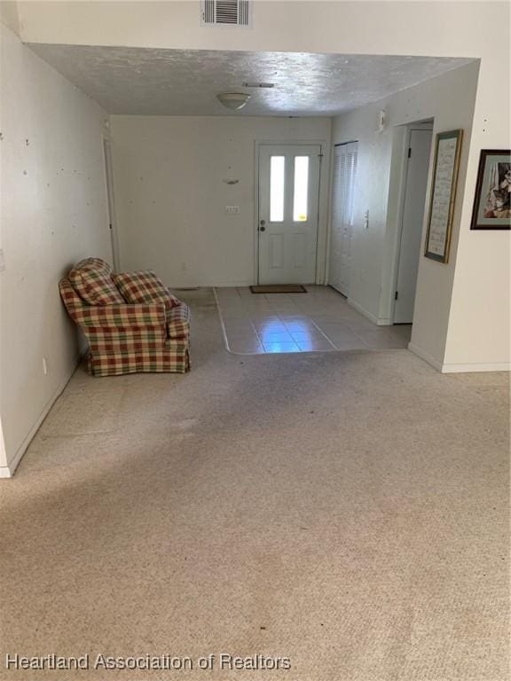 foyer featuring visible vents, baseboards, light colored carpet, a textured ceiling, and light tile patterned floors