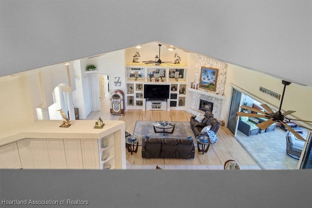 living room featuring built in shelves, light wood-type flooring, ceiling fan, and a premium fireplace