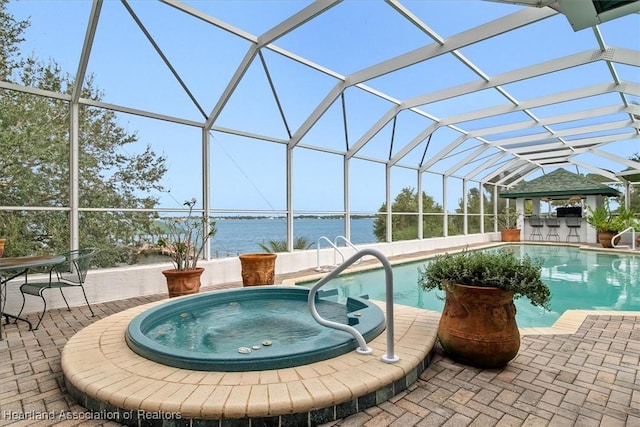 view of swimming pool with glass enclosure, a patio area, a water view, and a hot tub