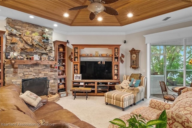 carpeted living room with a stone fireplace, a raised ceiling, ceiling fan, ornamental molding, and wood ceiling