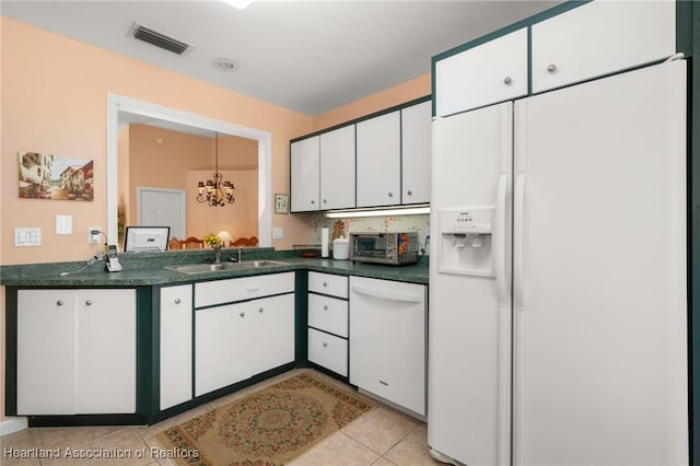 kitchen with visible vents, dark countertops, a sink, a notable chandelier, and white appliances