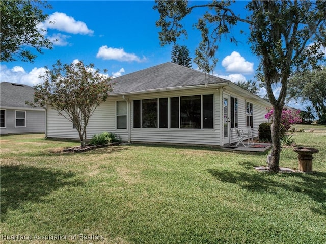 rear view of property featuring a lawn and a shingled roof