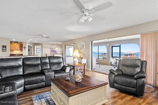 living room featuring ceiling fan, a water view, light hardwood / wood-style floors, and a textured ceiling