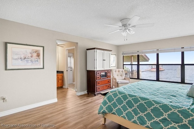 bedroom with ceiling fan, a water view, light hardwood / wood-style floors, and a textured ceiling