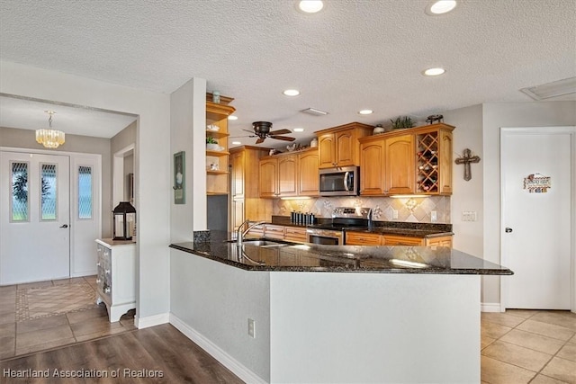 kitchen with a textured ceiling, appliances with stainless steel finishes, dark stone countertops, sink, and kitchen peninsula