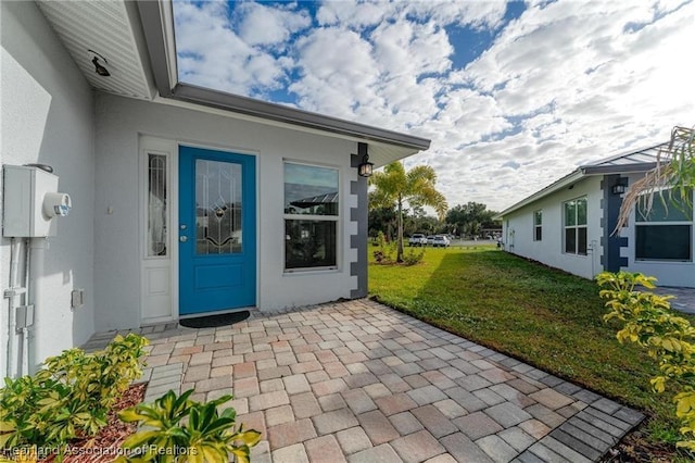 entrance to property featuring a patio and a lawn