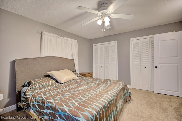 bedroom with a textured ceiling, ceiling fan, light carpet, and multiple closets