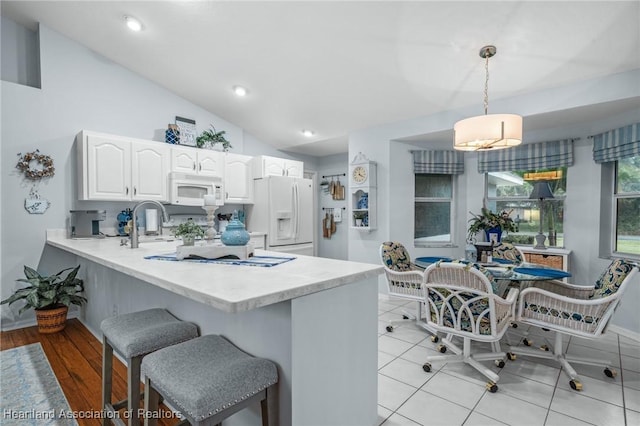 kitchen featuring kitchen peninsula, white appliances, vaulted ceiling, pendant lighting, and white cabinetry