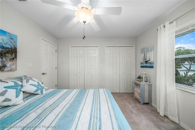 carpeted bedroom featuring ceiling fan, multiple closets, and multiple windows