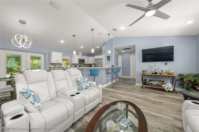 living room with french doors, light wood-type flooring, vaulted ceiling, visible vents, and ceiling fan with notable chandelier