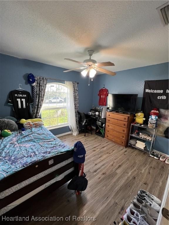 bedroom with hardwood / wood-style flooring, ceiling fan, and a textured ceiling