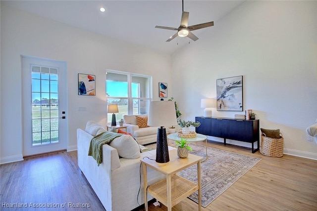 living room with ceiling fan, wood-type flooring, and a high ceiling