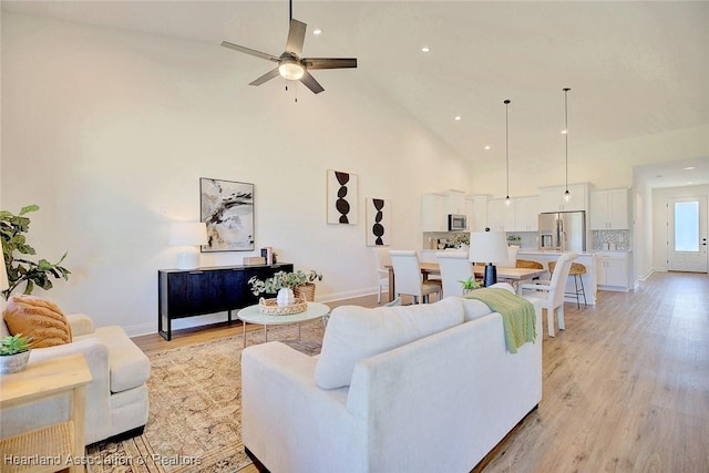 living room featuring high vaulted ceiling, ceiling fan, and light wood-type flooring