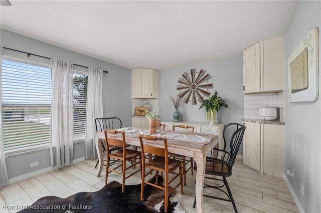 dining space featuring a textured ceiling, light wood-style floors, and baseboards
