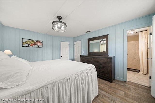 bedroom with connected bathroom, visible vents, and wood finished floors