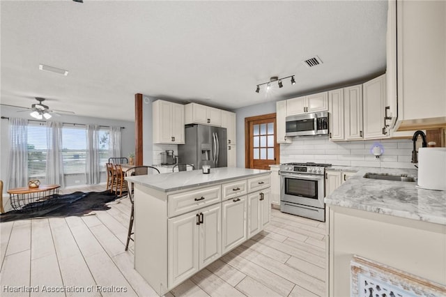 kitchen featuring a kitchen breakfast bar, a sink, visible vents, stainless steel appliances, and backsplash