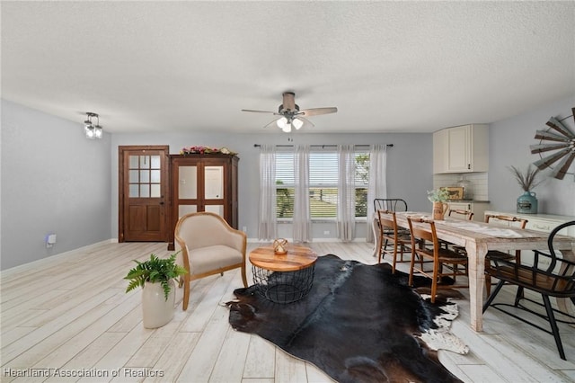 interior space with a textured ceiling, light wood-style floors, a ceiling fan, and baseboards