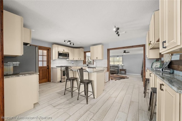 kitchen with a breakfast bar area, appliances with stainless steel finishes, backsplash, light wood finished floors, and a ceiling fan