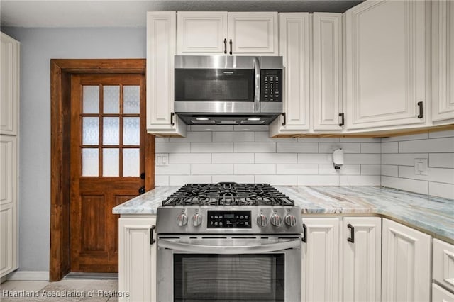 kitchen featuring stainless steel appliances, tasteful backsplash, light stone counters, baseboards, and white cabinets