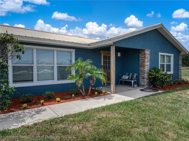 single story home featuring a front lawn, stucco siding, and metal roof