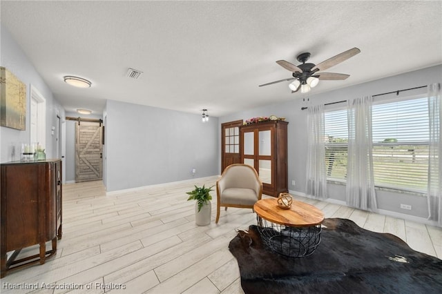 sitting room with a barn door, light wood-type flooring, baseboards, visible vents, and a ceiling fan