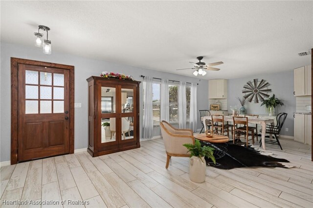 interior space featuring baseboards, visible vents, a ceiling fan, and light wood finished floors