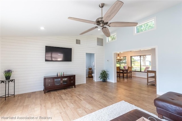 living room with light hardwood / wood-style floors, ceiling fan, lofted ceiling, and wood walls