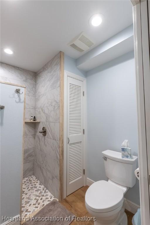bathroom with a tile shower, hardwood / wood-style flooring, and toilet