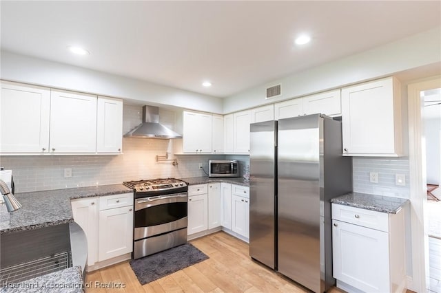 kitchen featuring white cabinets, wall chimney range hood, decorative backsplash, appliances with stainless steel finishes, and stone countertops
