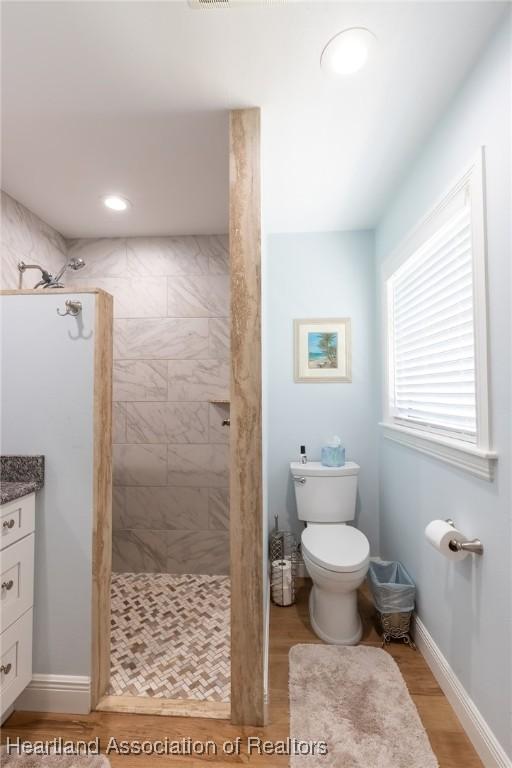 bathroom featuring hardwood / wood-style flooring, vanity, toilet, and a tile shower
