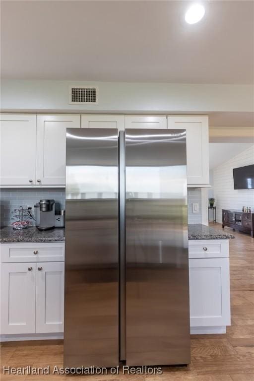 kitchen featuring light wood-type flooring, tasteful backsplash, dark stone counters, white cabinets, and stainless steel refrigerator