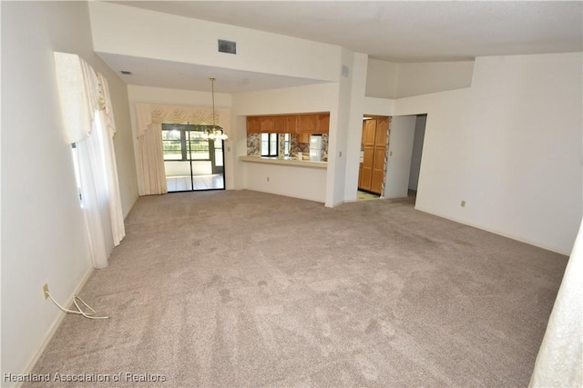 unfurnished living room featuring a notable chandelier, light carpet, and high vaulted ceiling