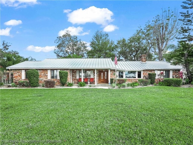 ranch-style home with brick siding, a chimney, metal roof, and a front yard